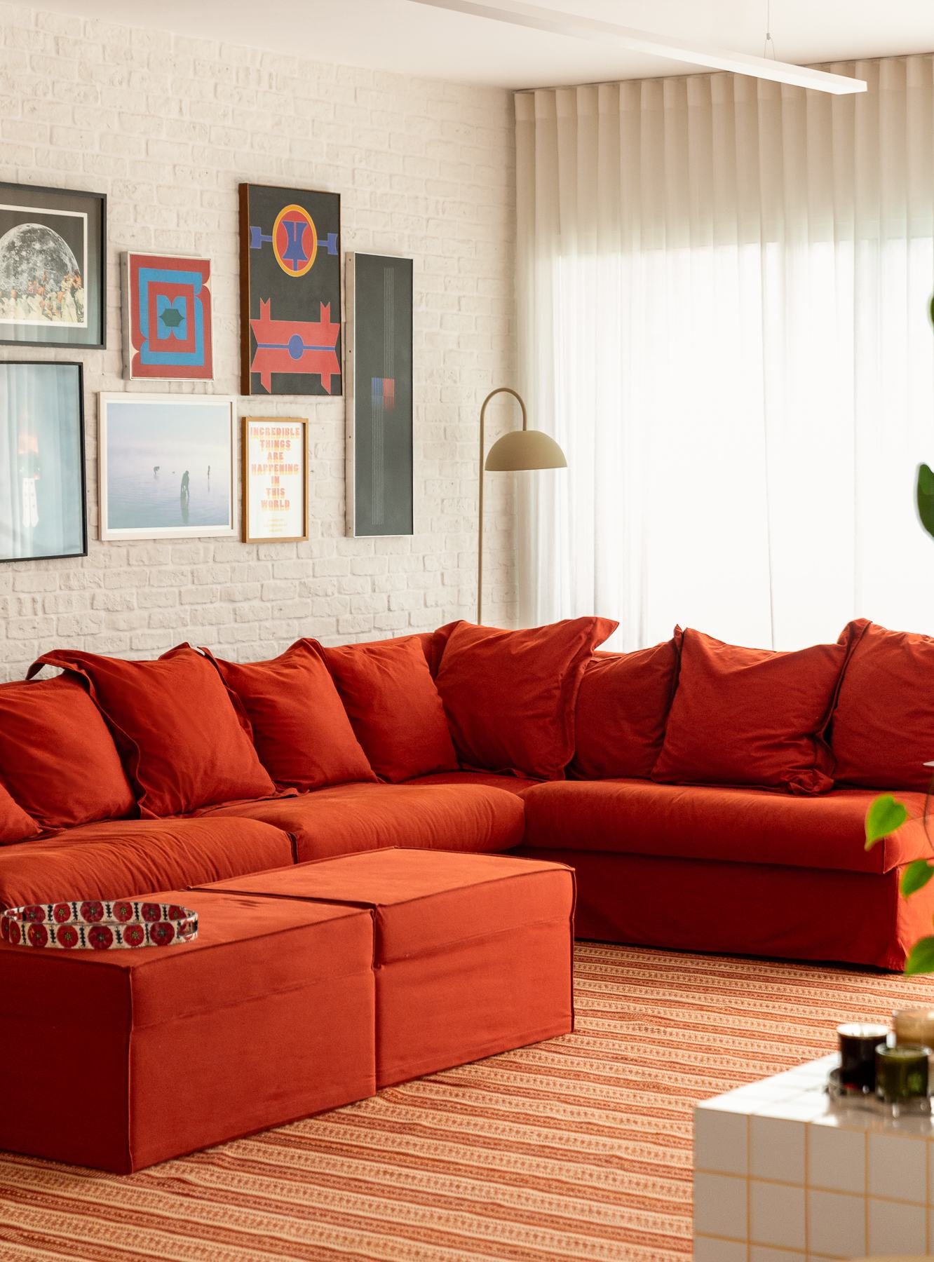 Sala com sofá vermelho, parede-galeria de quadros e cortinas claras