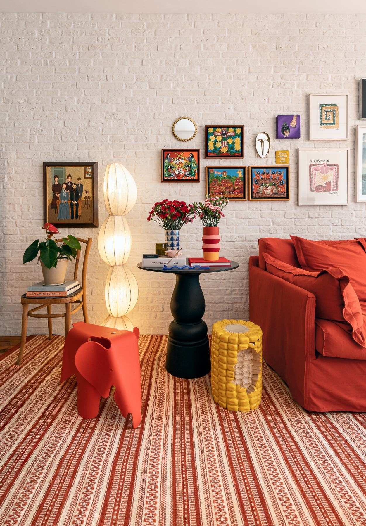Sala de estar com sofá vermelho, luminárias de piso e mesa lateral preta sobre tapete listrado