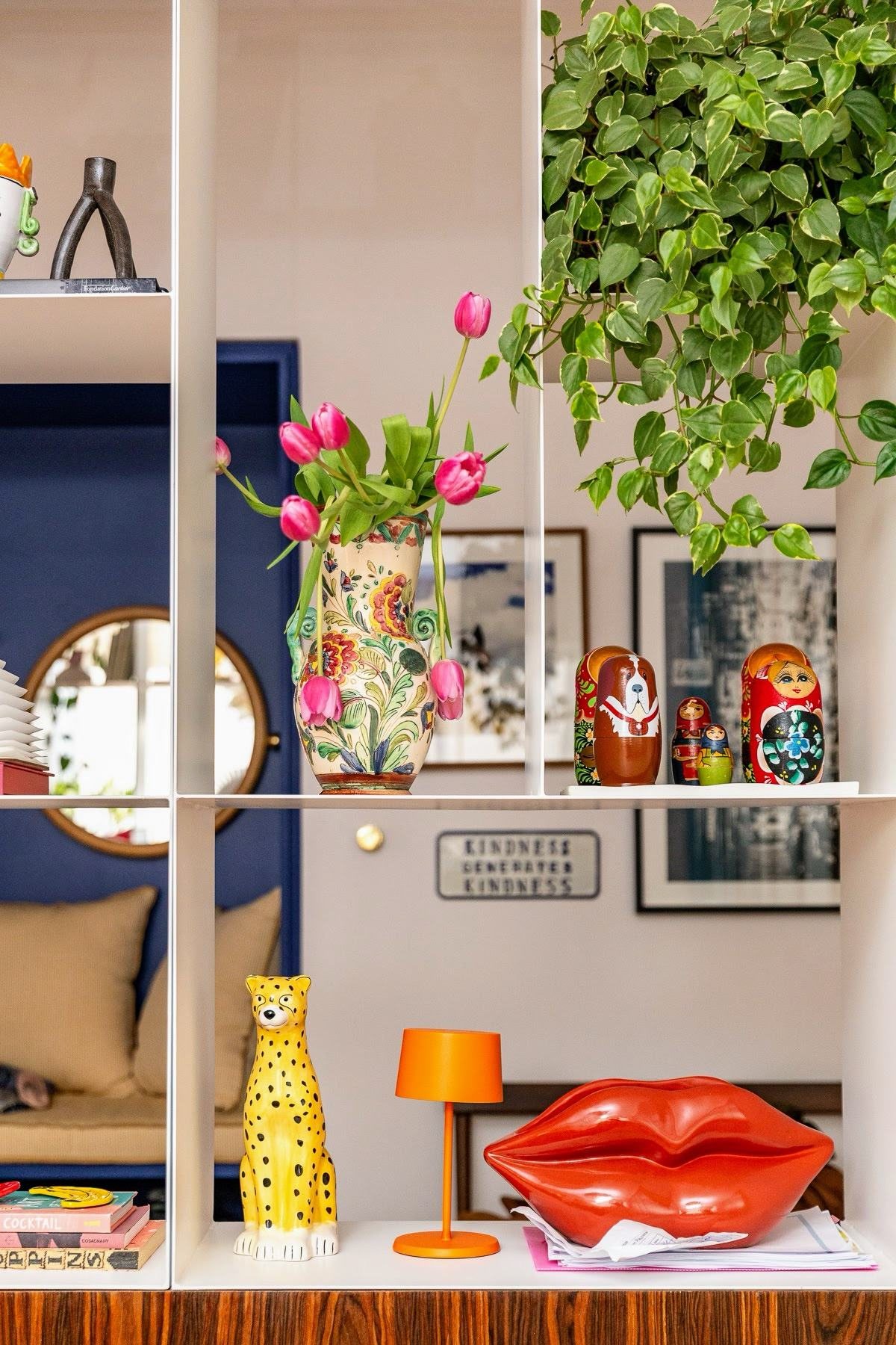 Estante com vaso de tulipas, bonecas russas, luminária laranja e sofá em forma de lábios vermelhos