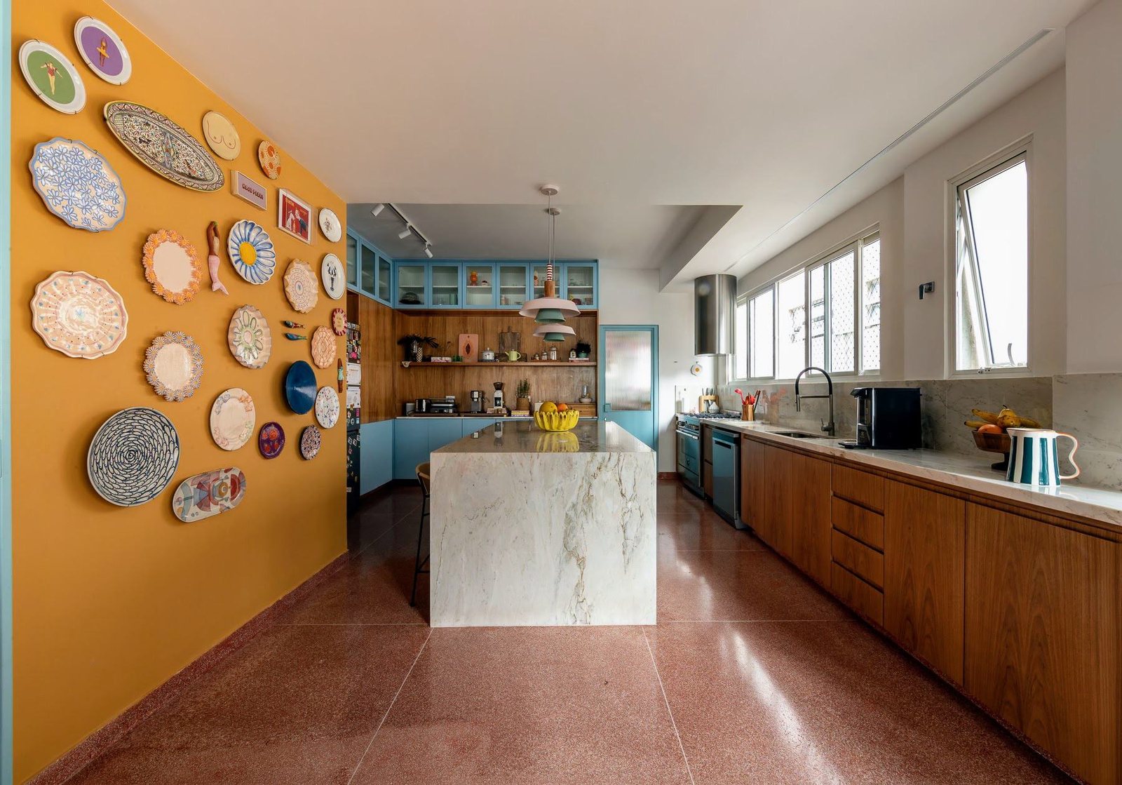 Cozinha com parede amarela coberta de pratos decorativos, ilha de mármore e marcenaria de madeira